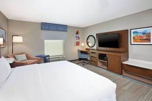 A hotel room with a large bed, a desk with a chair, a flat-screen TV, a mirror, and framed pictures on the wall.