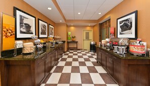 A hotel kitchen with a checkered floor, framed pictures on the walls, and various food and drink stations.