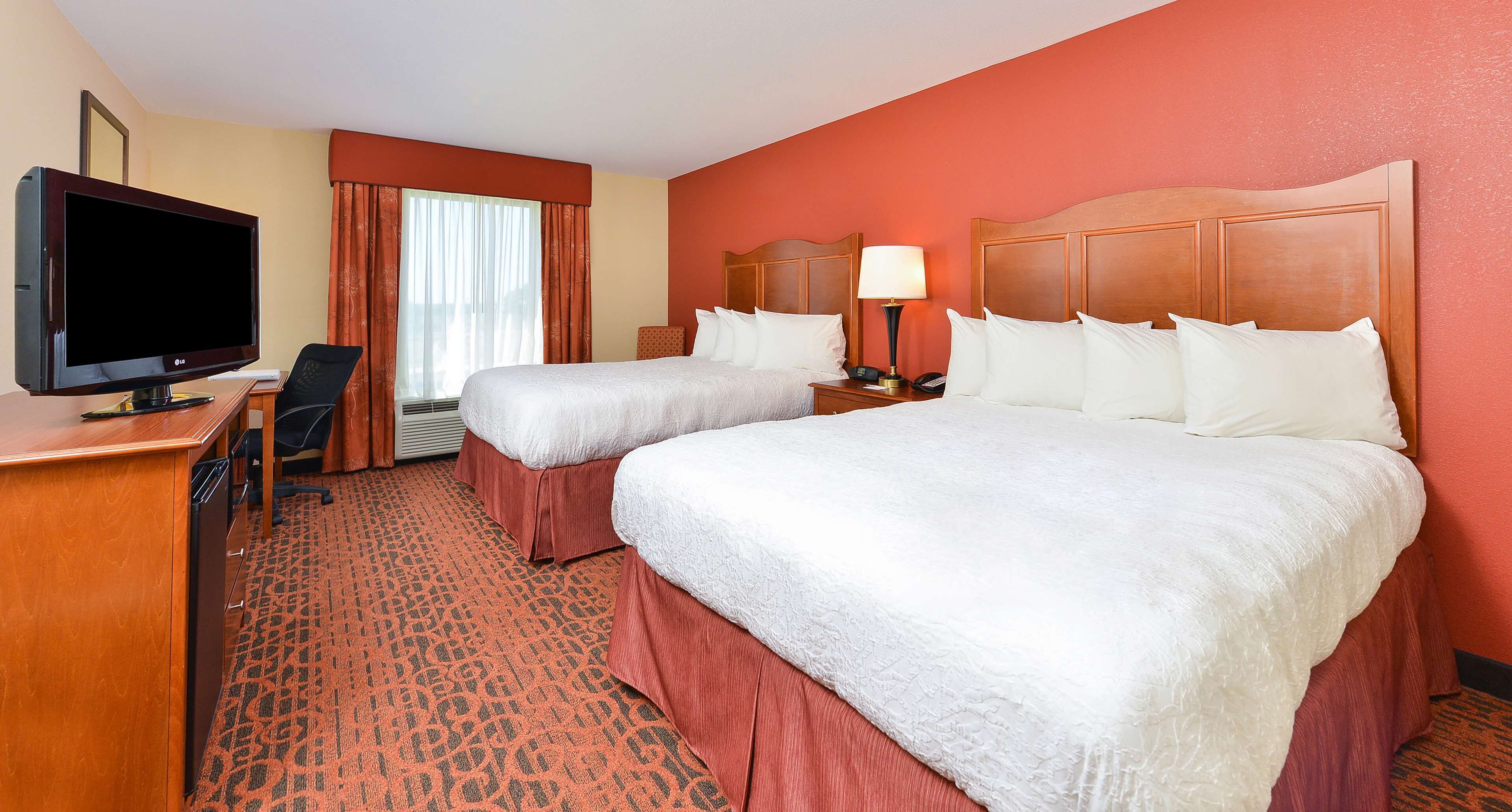 A hotel room with two beds, a desk with a television, a chair, a lamp, and a telephone.