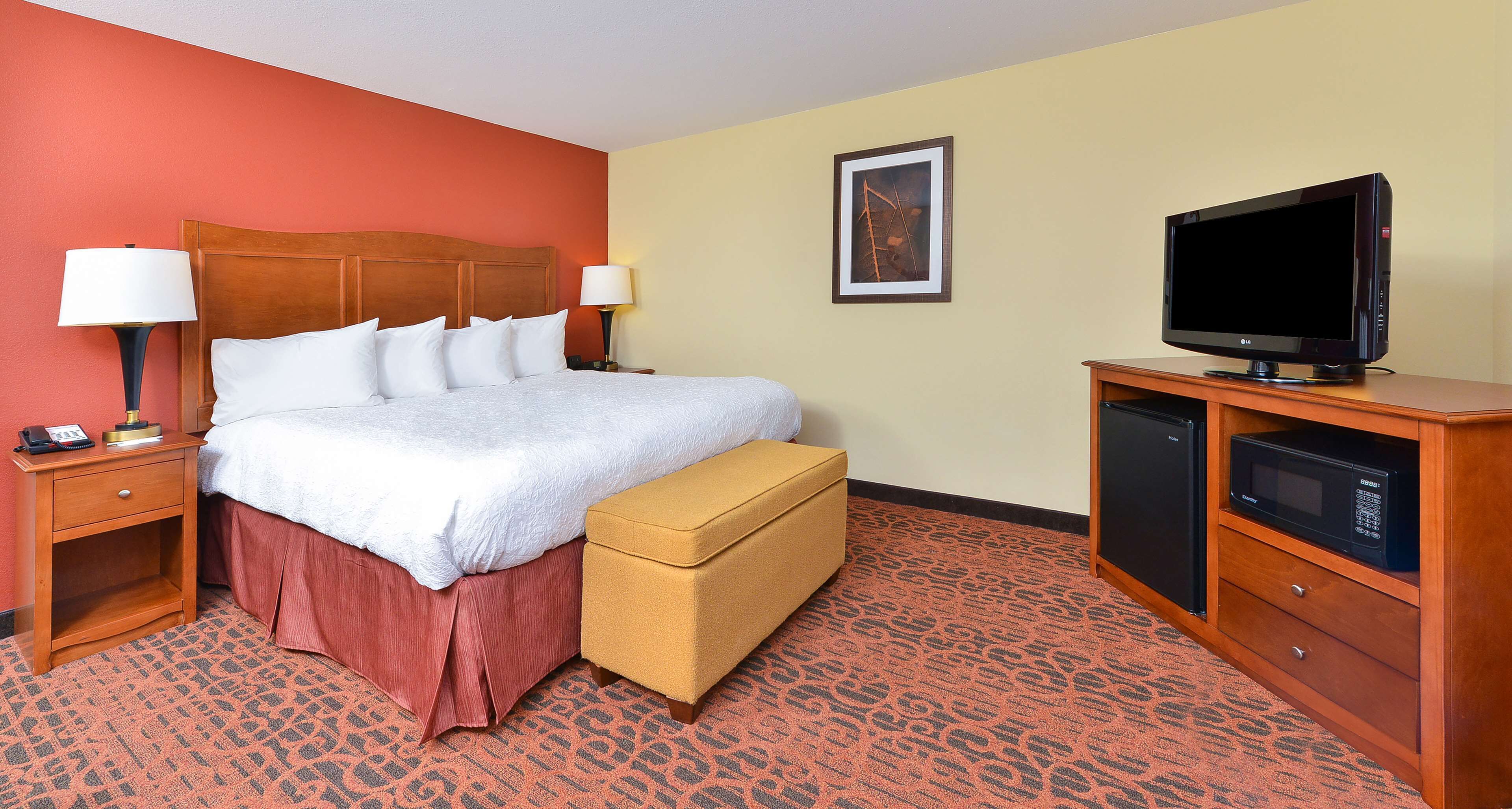 Habitación de hotel con cama, lámparas de noche, televisor, microondas y una pequeña mesa con teléfono.