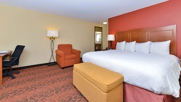 A hotel room with a large bed, a desk, an orange armchair, and a small sofa.