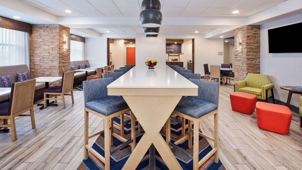 A modern meeting room with a large table, comfortable seating, and a stone accent wall. - Hampton Inn Clinton, IA (Clinton)