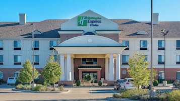 A Holiday Inn Express & Suites hotel with a brick facade, a central entrance with a covered porch, and a parking lot with several cars.