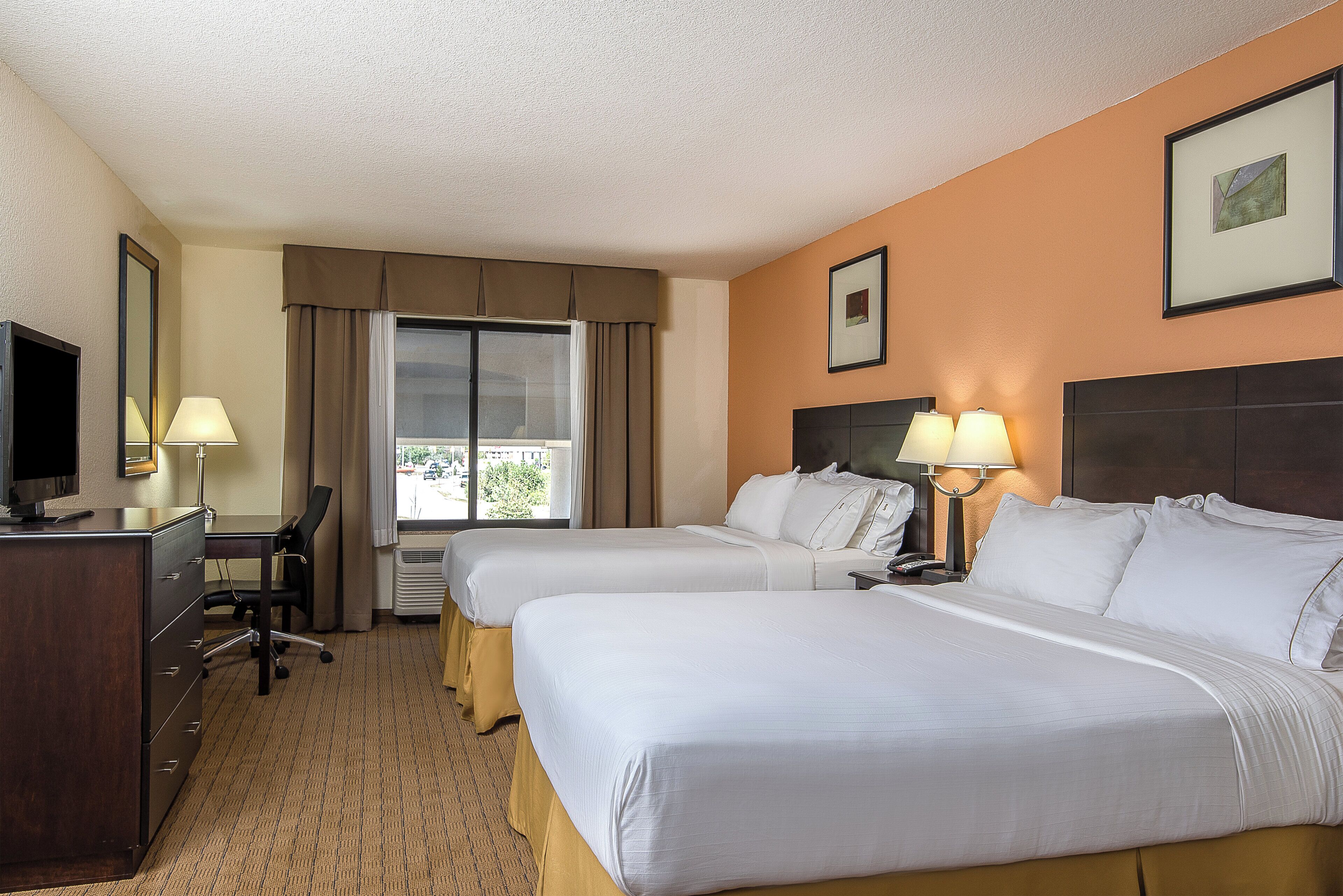A hotel room with two beds, a desk, a chair, a TV, and a window with curtains.