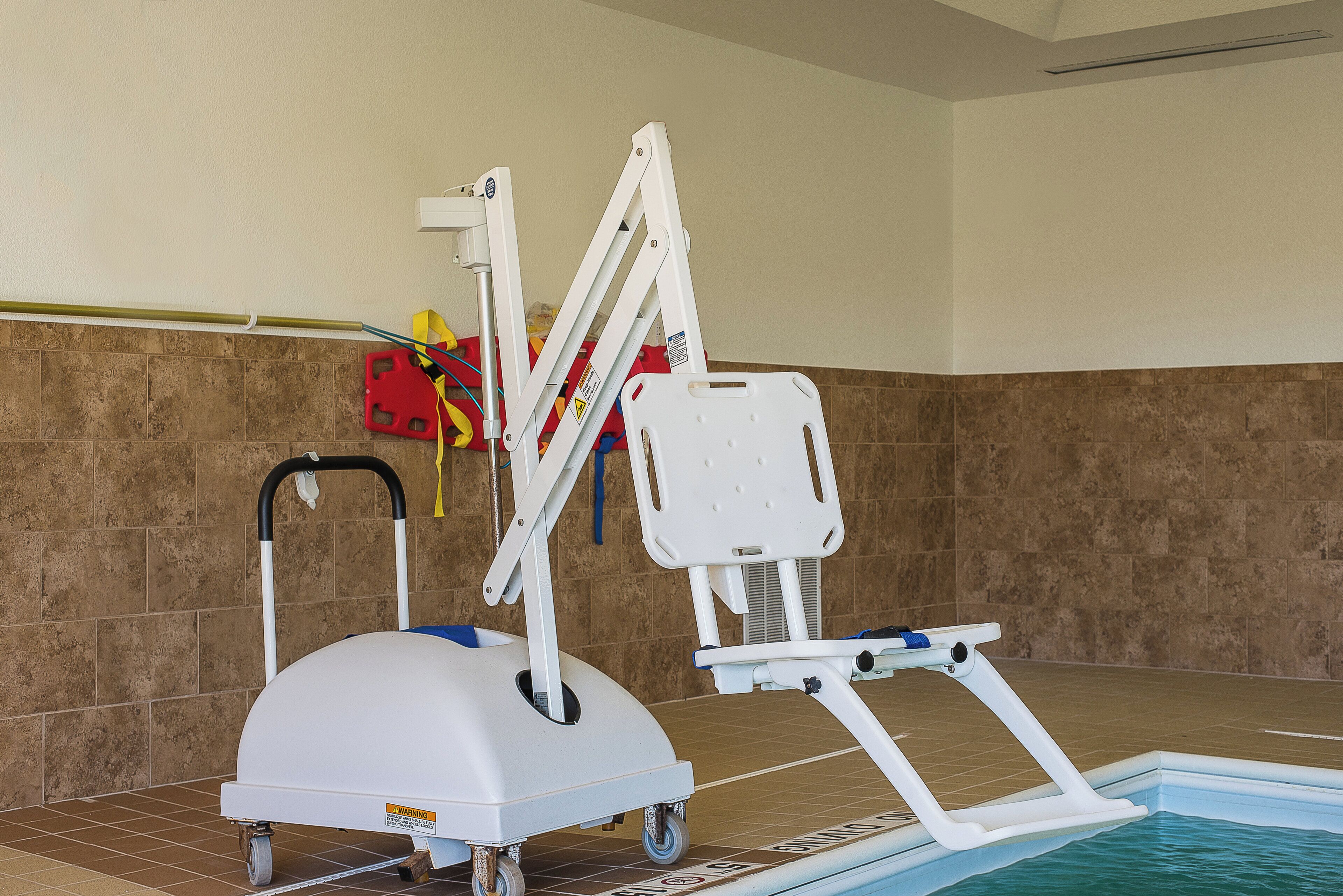 A pool lift chair with wheels, a red safety flotation device, and a white pool ladder.