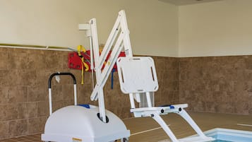 A pool lift chair with wheels, a red safety flotation device, and a white pool ladder.