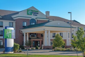 Un hôtel Holiday Inn Express & Suites avec une façade en briques, une entrée abritée et un ciel d’un bleu limpide.