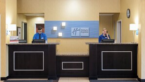 A hotel reception desk with two receptionists, a clock, and a Holiday Inn Express sign. - Holiday Inn Express & Suites Lafayette East by IHG (Lafayette)