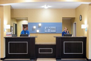 A hotel reception desk with two receptionists, a clock, and a Holiday Inn Express sign. - Holiday Inn Express & Suites Lafayette East by IHG (Lafayette)