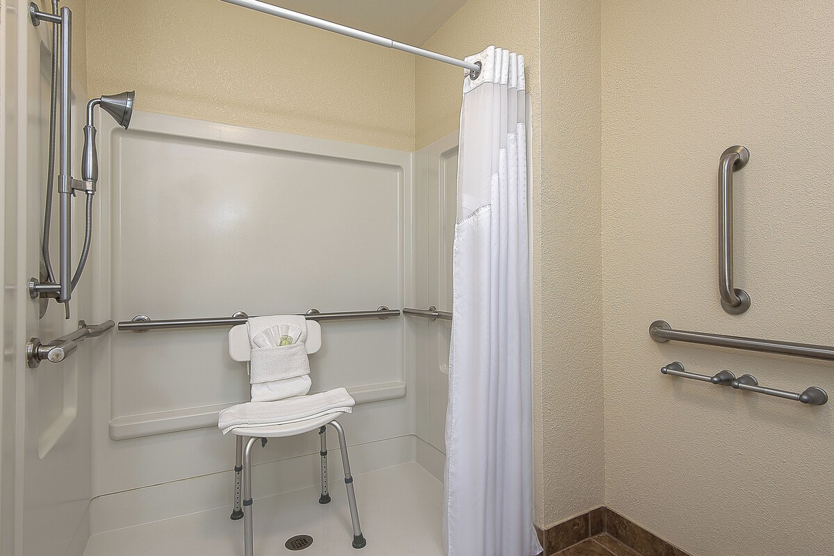 A bathroom with a shower, grab bars, a white toilet, and a towel rack.