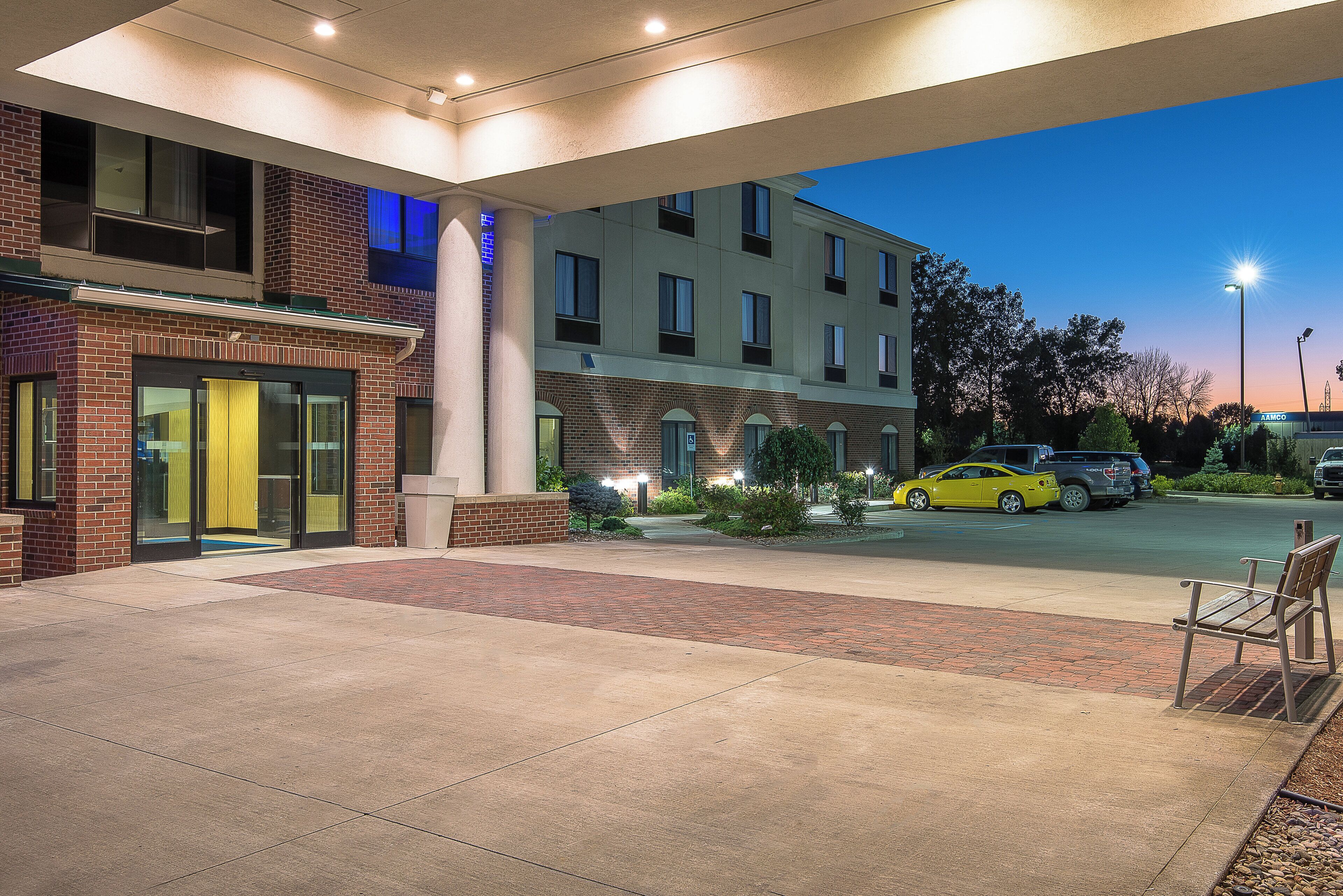 A hotel entrance with a brick facade, a yellow car parked in front, and a clear sky.