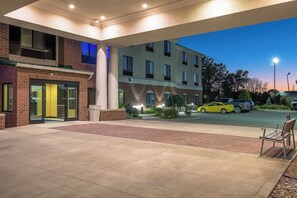 En hotels entré med en murstensfacade, en gul bil parkeret foran, og en klar himmel.
