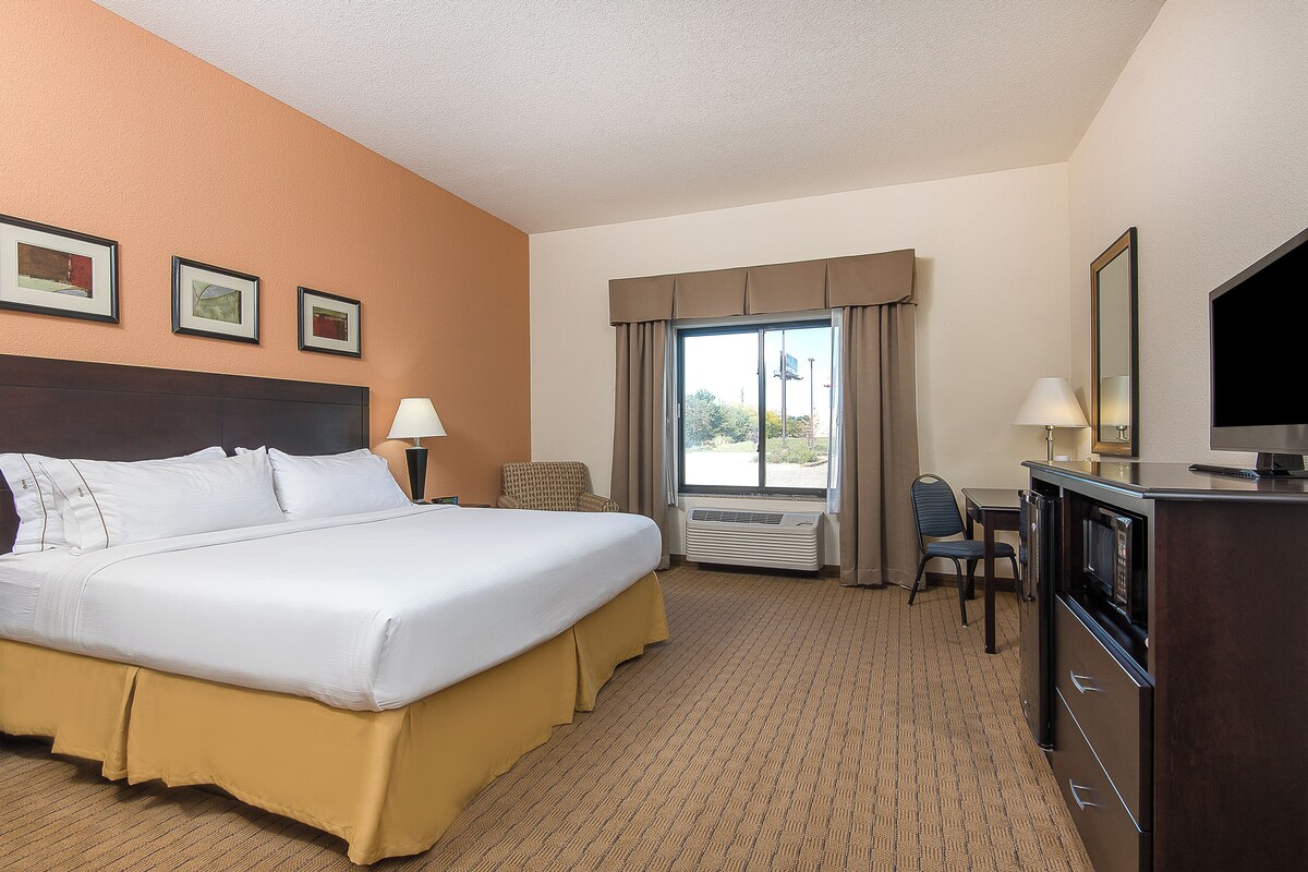 A hotel room with a bed, a desk, a chair, a TV, and a window with curtains.
