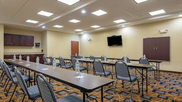 Un salón de conferencias con varias mesas y sillas, equipado con botellas de agua, un televisor de pantalla plana y un sistema de sonido integrado.