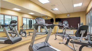 Un gimnasio con cintas de correr, bicicletas estáticas y pesas.