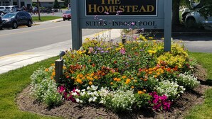 A sign for The Homestead Suites & Indoor Pool, surrounded by colorful flower beds. - Homestead Suites (Fish Creek)