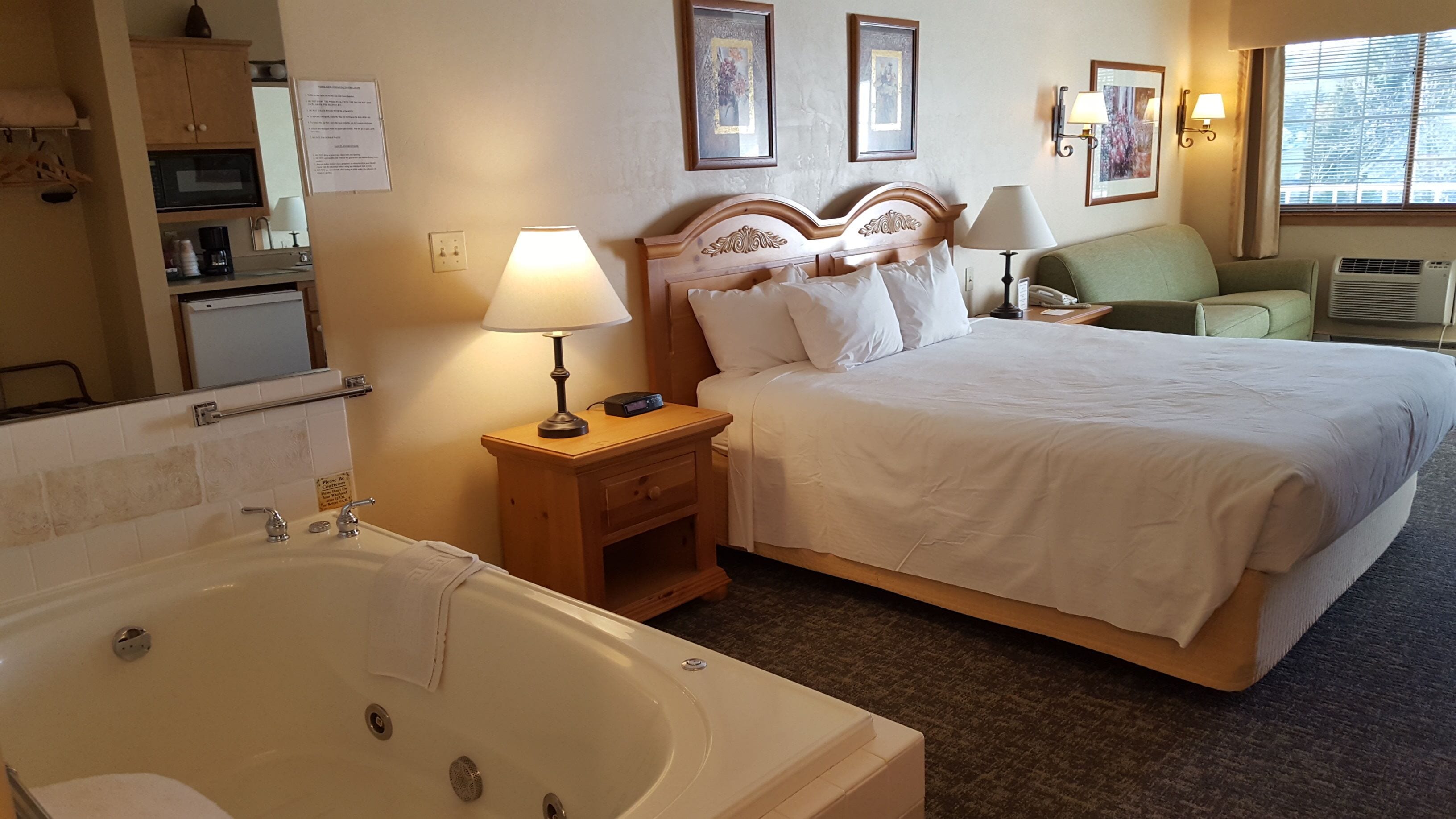 Hotelkamer met een groot bed, een eigen badkamer met bad, een klein bureau en een groene fauteuil.