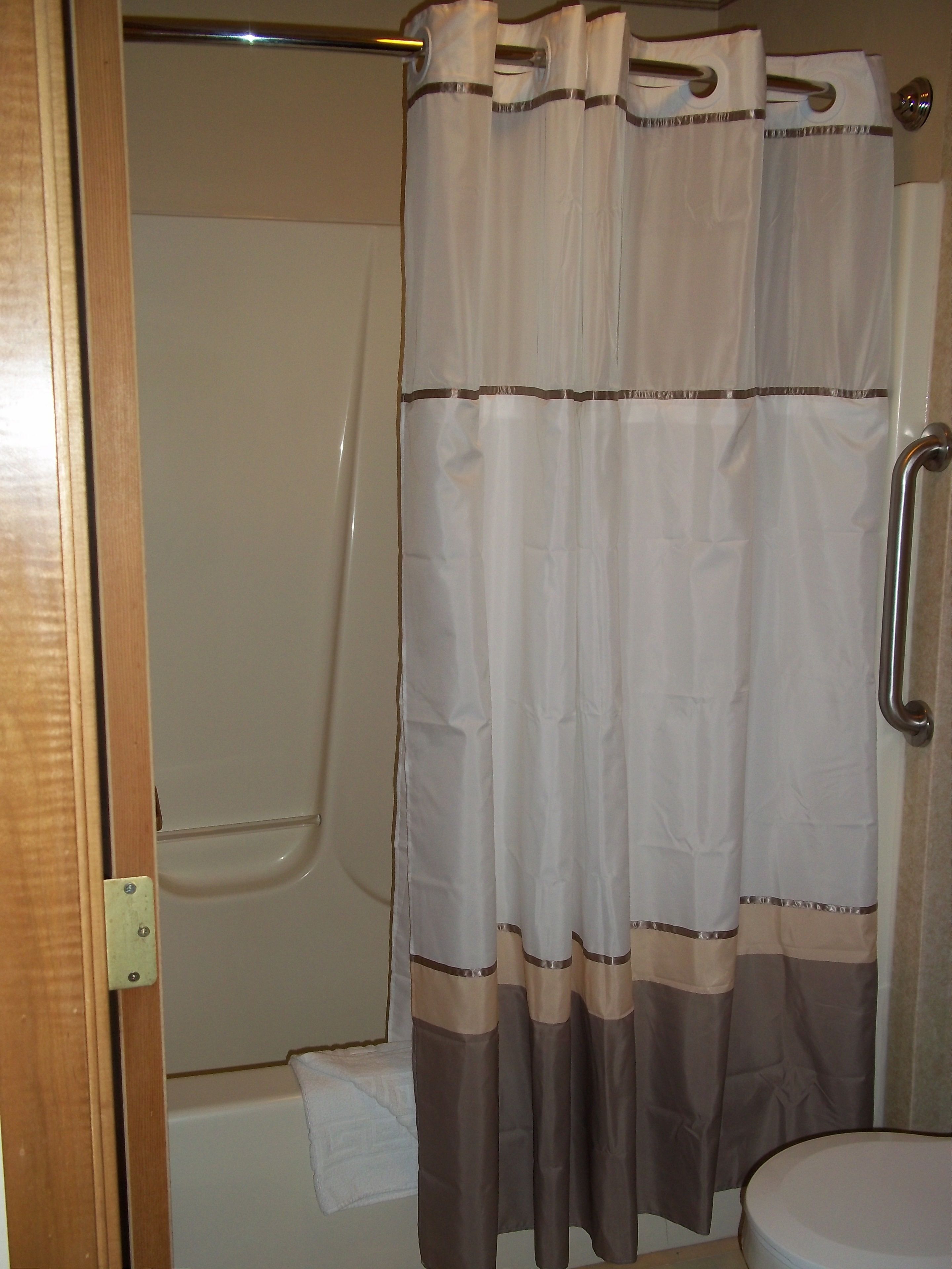 Ein Badezimmer mit Duschvorhang, Haltegriff und weißer Toilette.