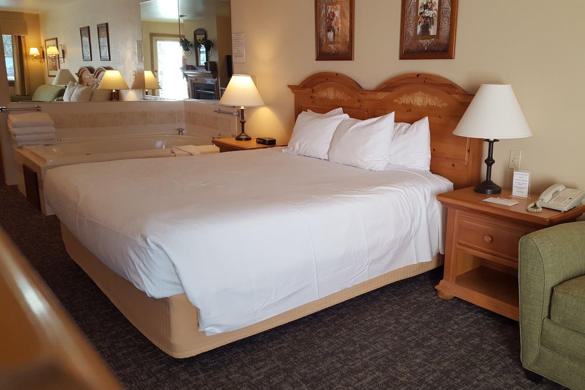 A hotel room with a large bed, two bedside tables, a green armchair, and a mirror reflecting the room.