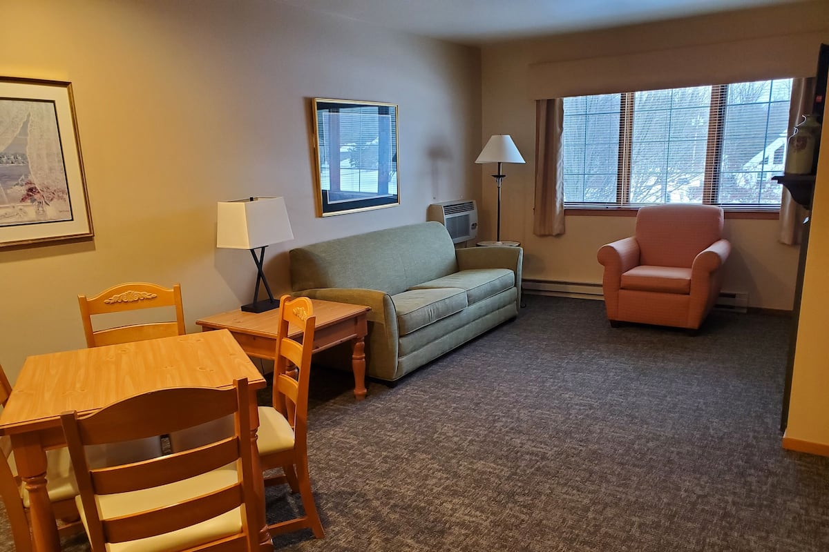 A living room with a sofa, a table, chairs, a lamp, and a window with blinds.