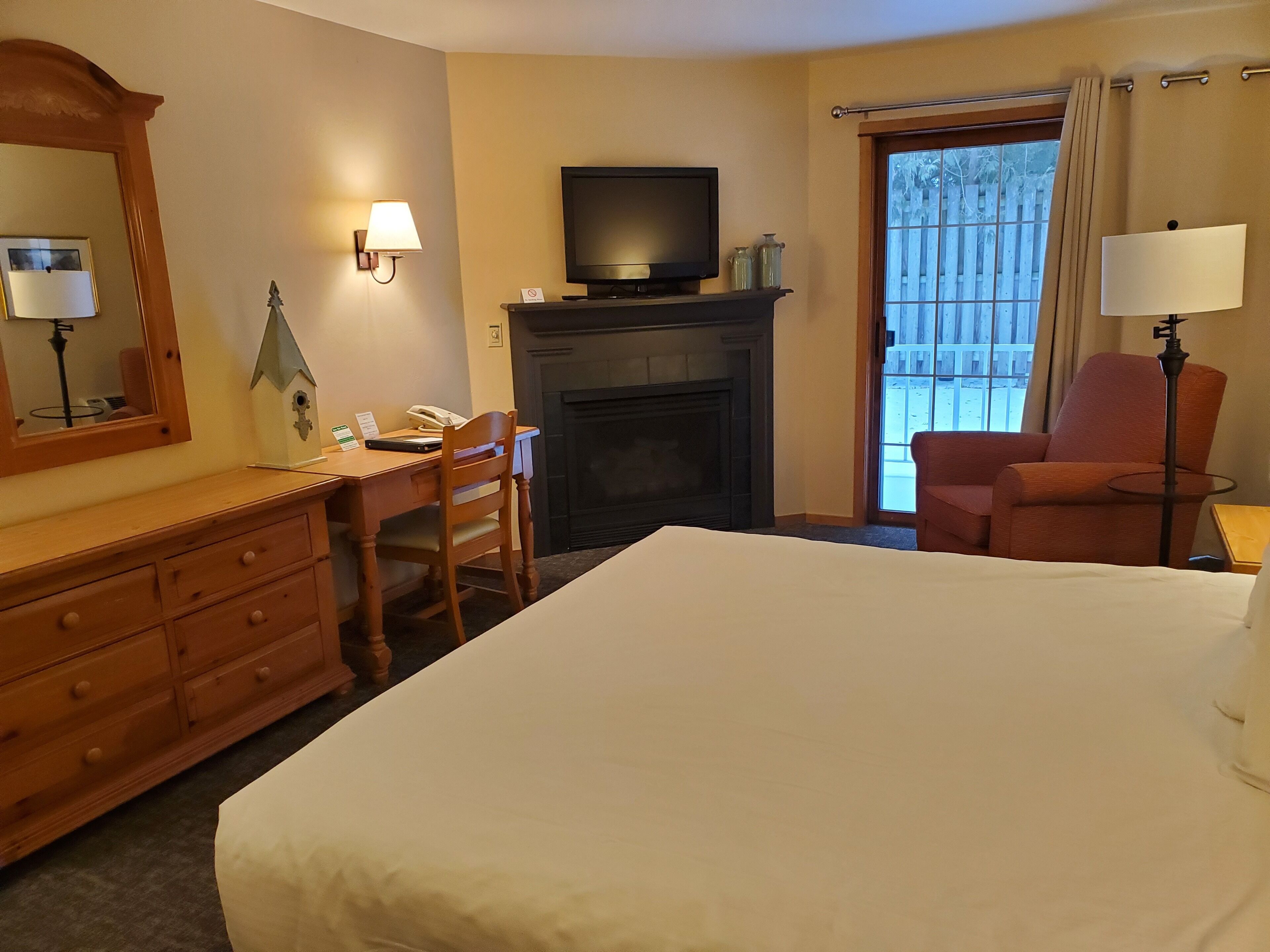 Habitación de hotel con cama, escritorio con silla, televisor, chimenea, espejo y ventana con cortinas.