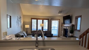 A modern kitchen with a double sink, a dining area with a sofa and chairs, a fireplace, and a TV mounted on the wall. - Homestead Suites (Fish Creek)