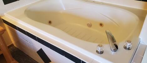 A large, rectangular bathtub with a single faucet, surrounded by white and black tiles.