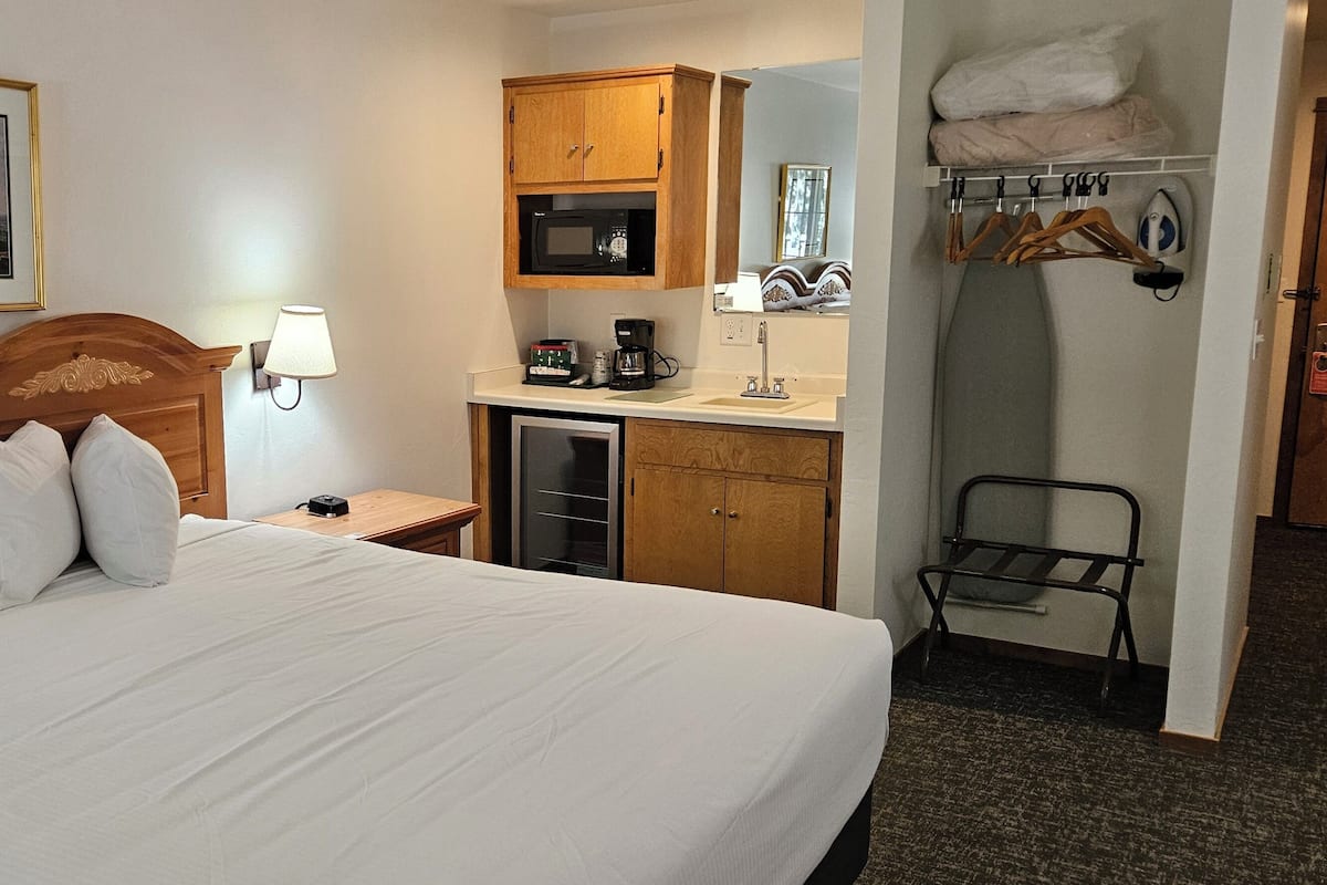 A hotel room with a bed, a desk with a lamp, a microwave, a coffee maker, and a closet with hanging clothes.