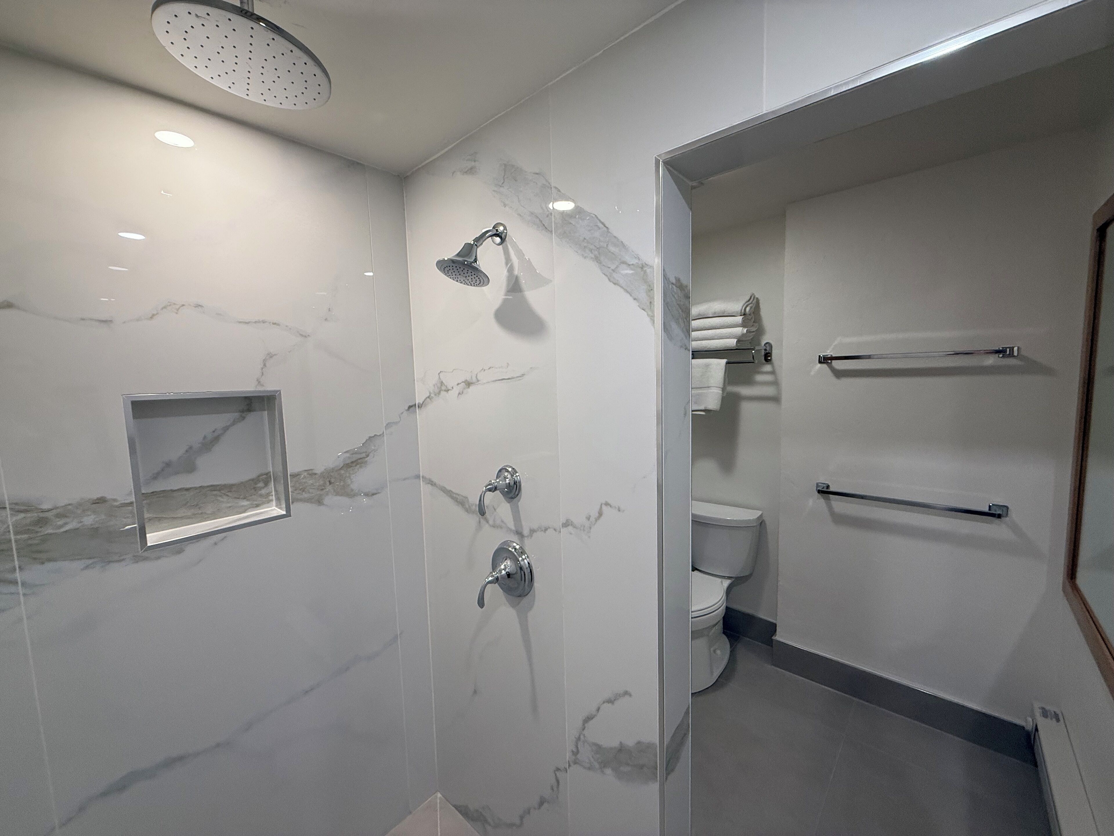 A modern bathroom with a shower, toilet, and towel rack.