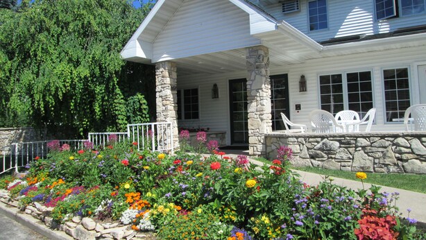 A white house with a stone porch, a garden with colorful flowers, and a clear blue sky. - Homestead Suites (Fish Creek)