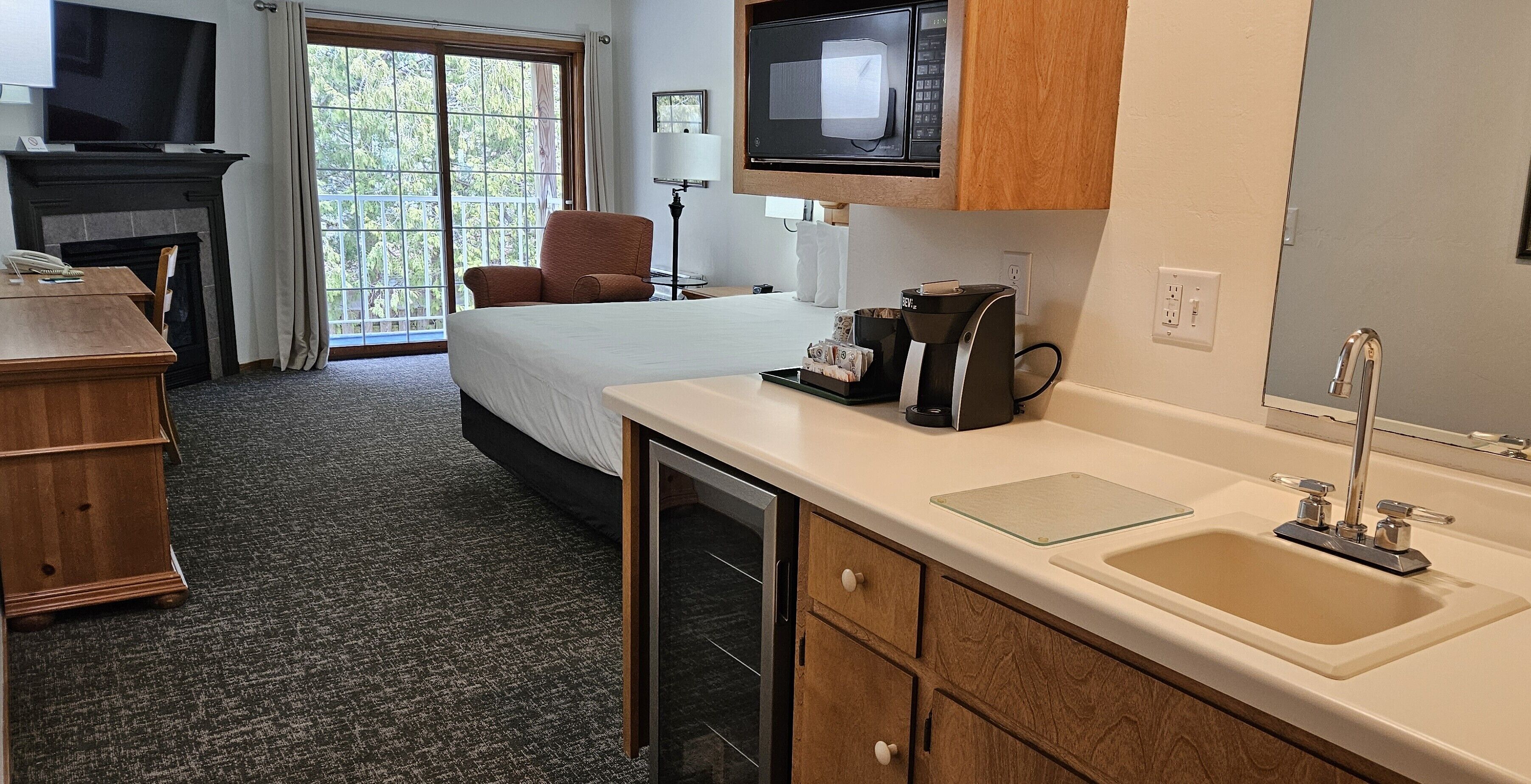Habitación de hotel con cama, escritorio, televisión, microondas, cafetera y lavamanos.
