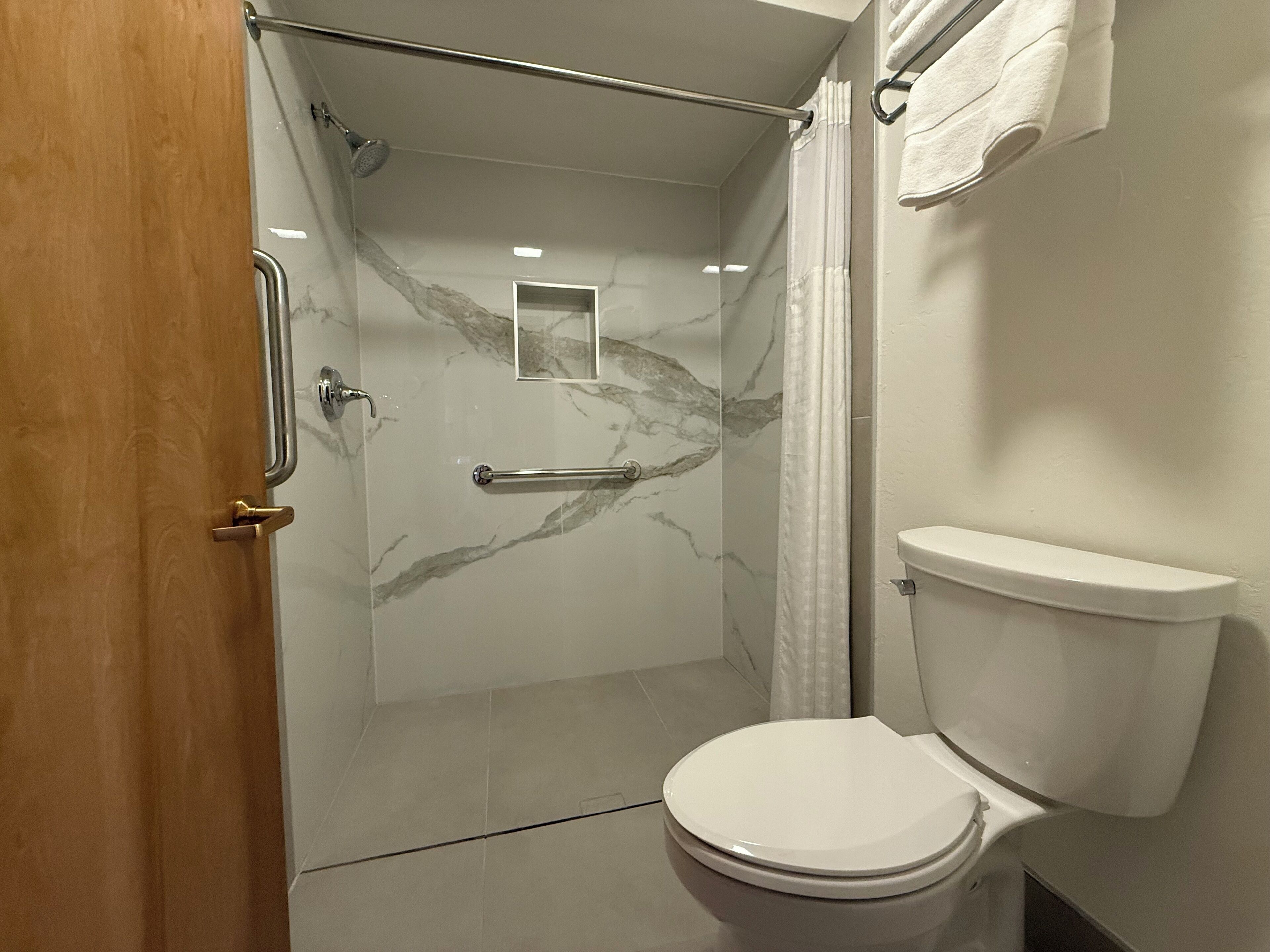 Un baño con cabina de ducha de vidrio, inodoro blanco y salpicadero de mármol.