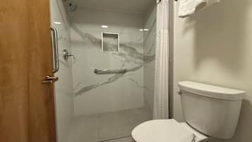 Un baño con cabina de ducha de vidrio, inodoro blanco y salpicadero de mármol.