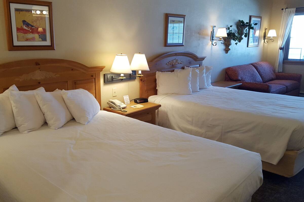 A hotel room with two beds, a wooden headboard, a nightstand with a phone, and a red couch.