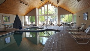 An indoor swimming pool with a wooden ceiling, large windows, and lounge chairs. - Homestead Suites (Fish Creek)