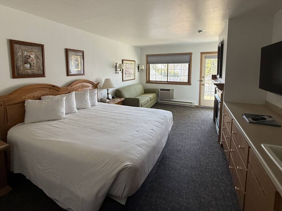 A hotel room with a large bed, a sofa, a TV, and a desk with a lamp.
