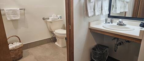A bathroom with a toilet, a sink, a mirror, and a basket of towels.