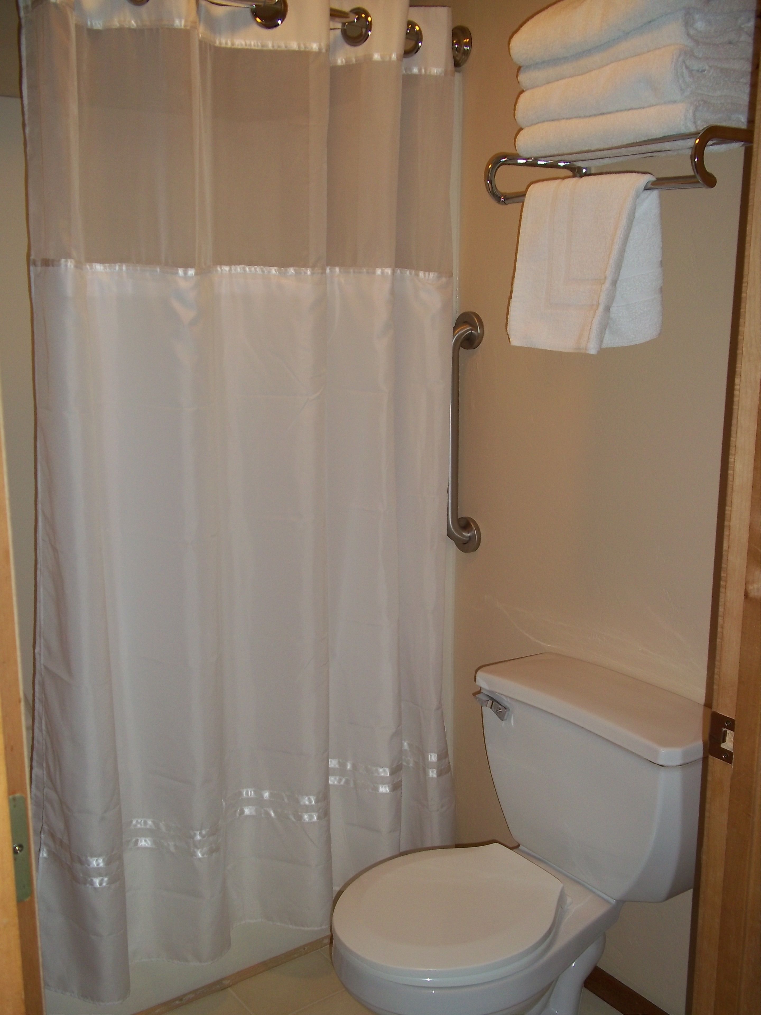 Een badkamer met een toilet, douchegordijn en een handdoekrek met opgevouwen handdoeken.