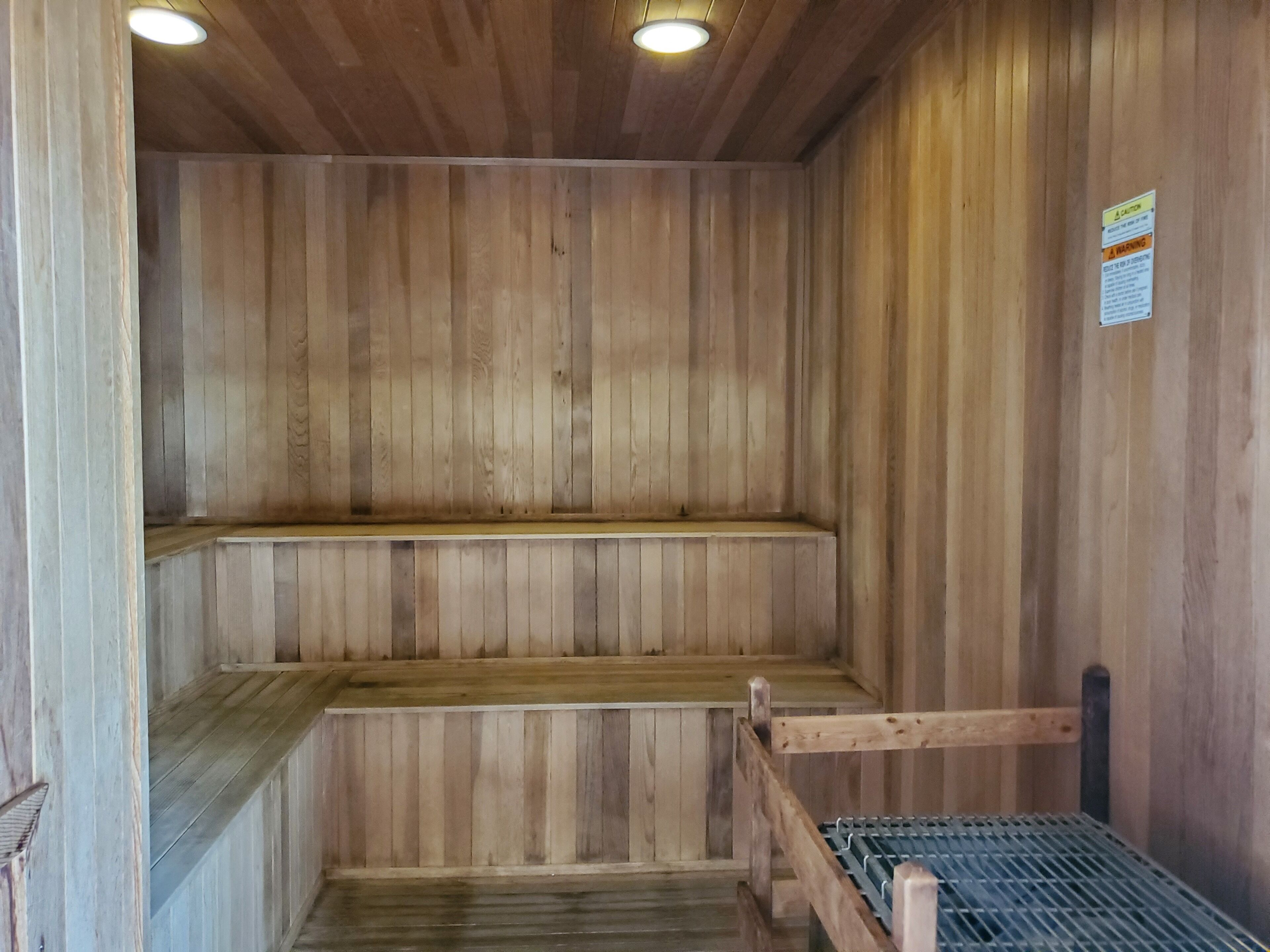 A sauna with wooden walls and benches, a metal grate floor, and a caution sign on the wall.