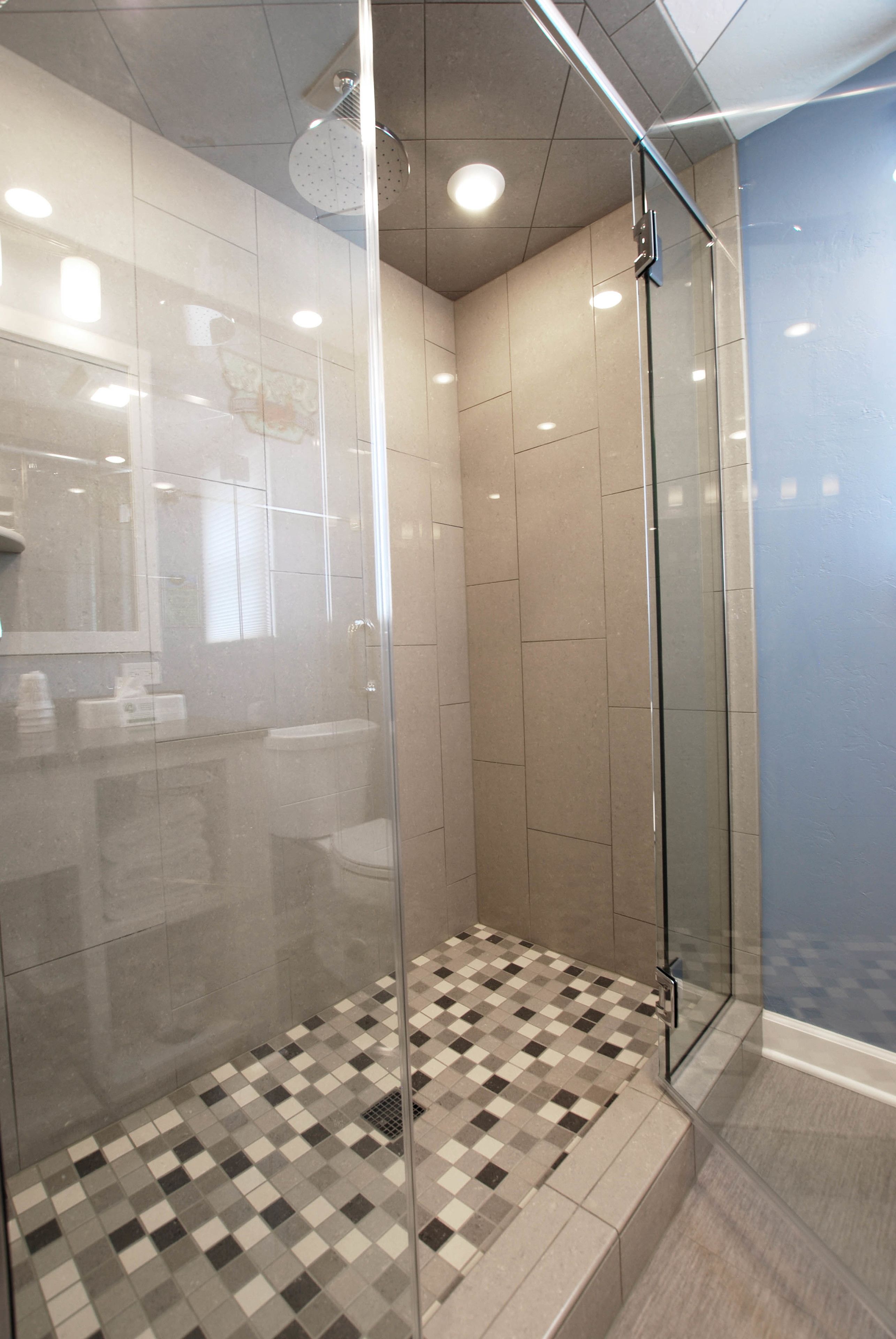 A modern bathroom with a glass-enclosed shower, checkered floor tiles, and a visible toilet.