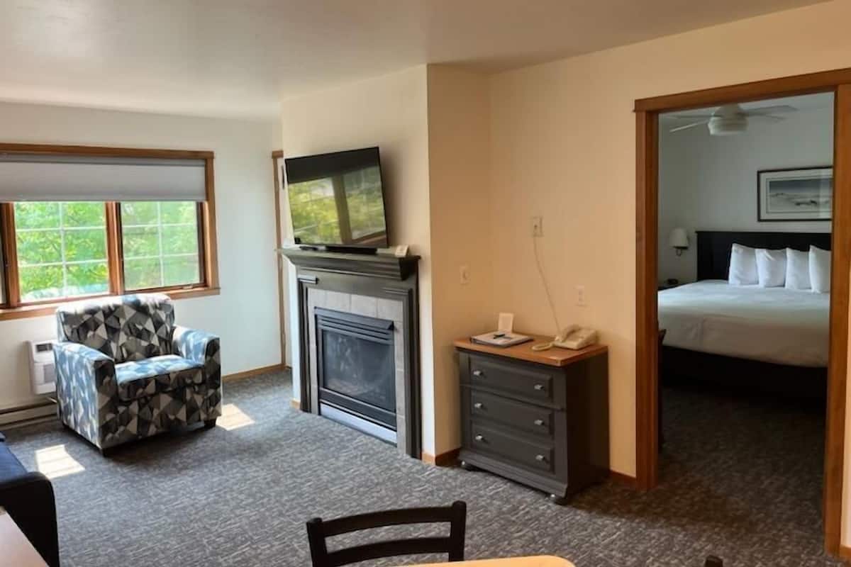 A hotel room with a fireplace, a television, a desk with a telephone, a bed, and a chair.