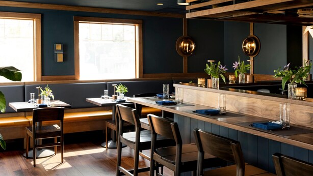 A restaurant interior with wooden bar stools, a high counter, and a large window.
