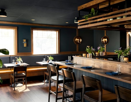 A restaurant interior with wooden bar stools, a high counter, and a large window.. Grand Hotel
