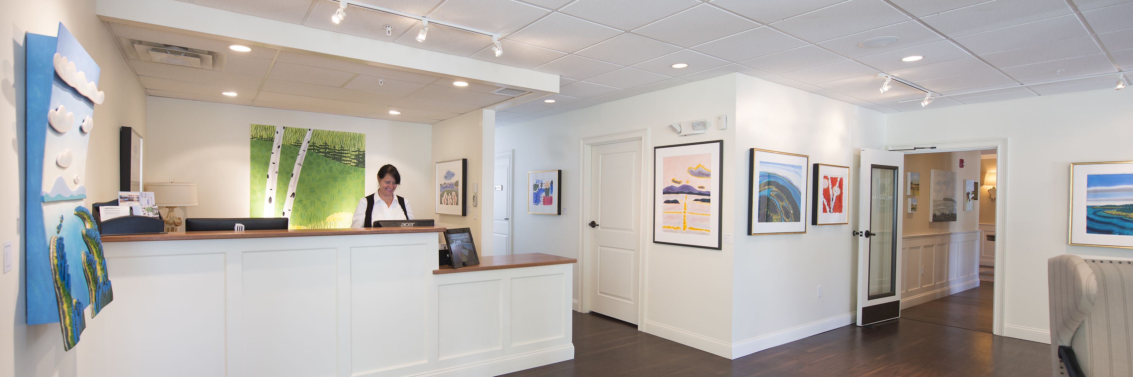 A reception area with a wooden reception desk, framed artwork on the walls, and a door leading to another room.