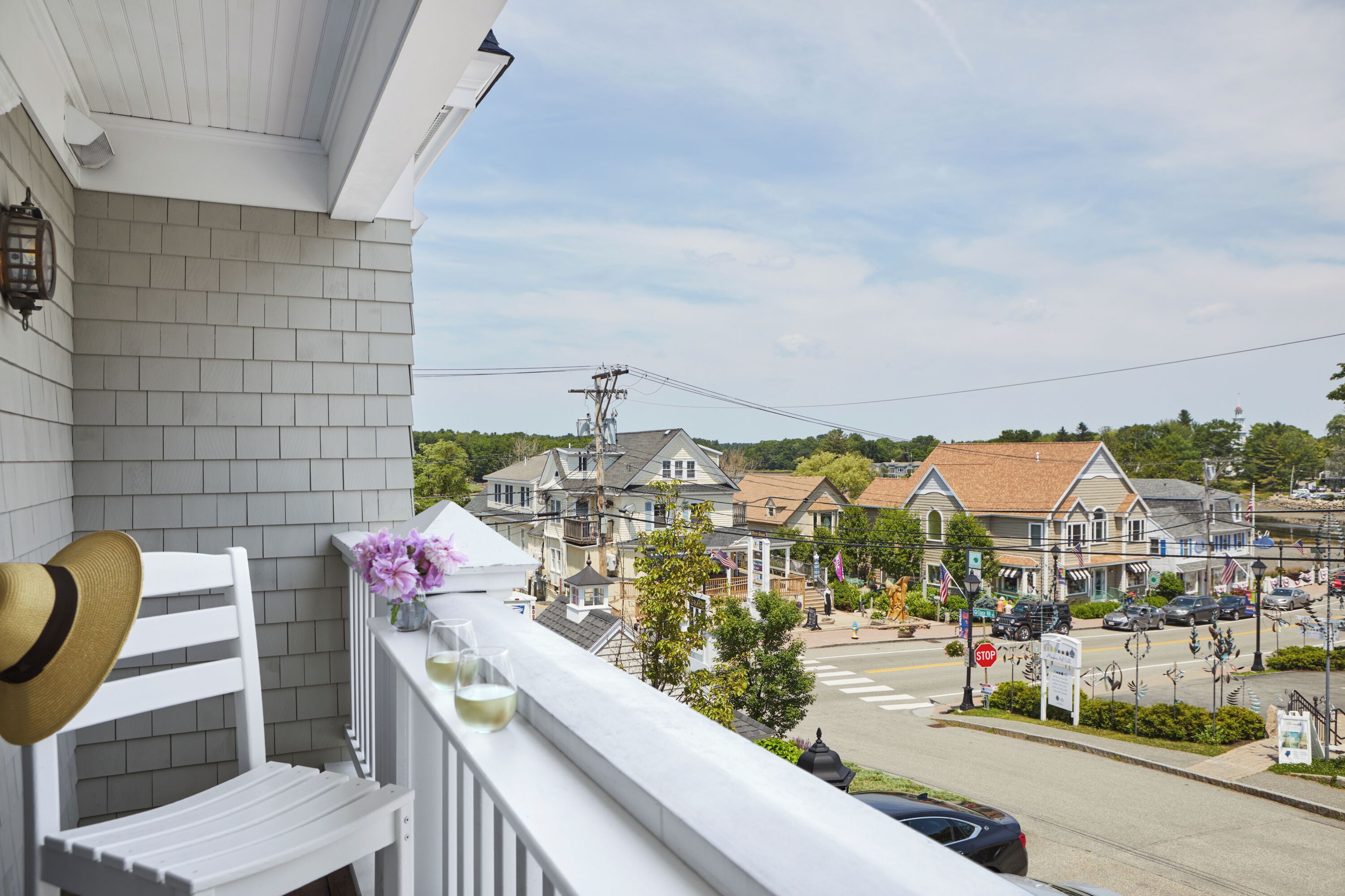 A balcony with a white chair, a hat, and a vase with flowers.