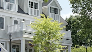 A two-story house with a balcony, a stone staircase, and a garden with flowers and plants.