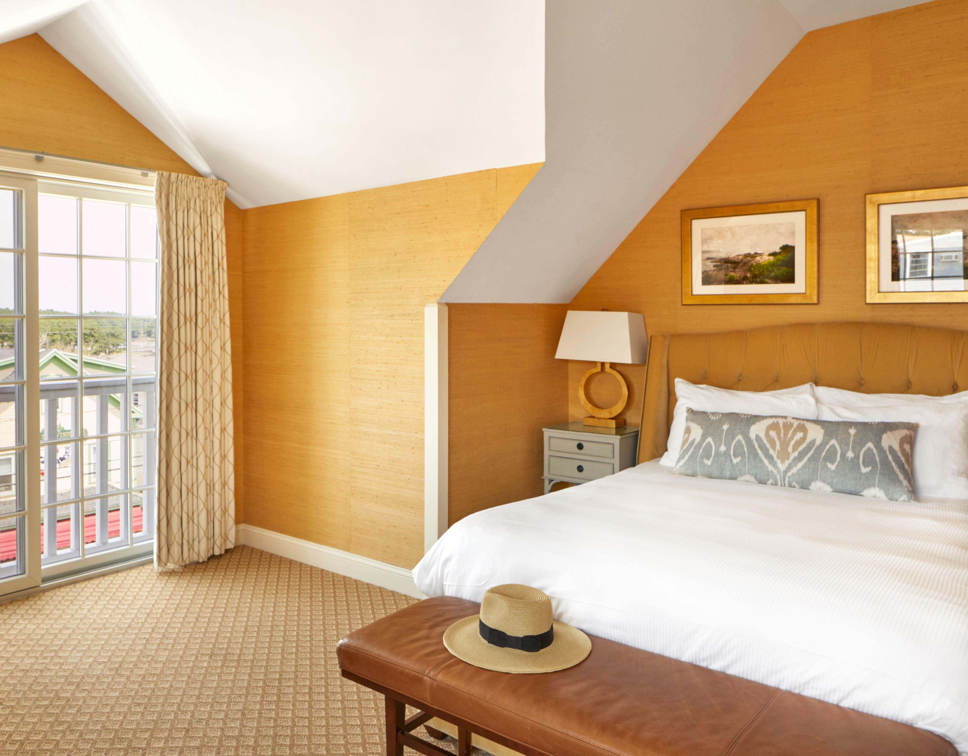 A hotel room with a large bed, a nightstand, a lamp, a window with curtains, and a view of the outside.