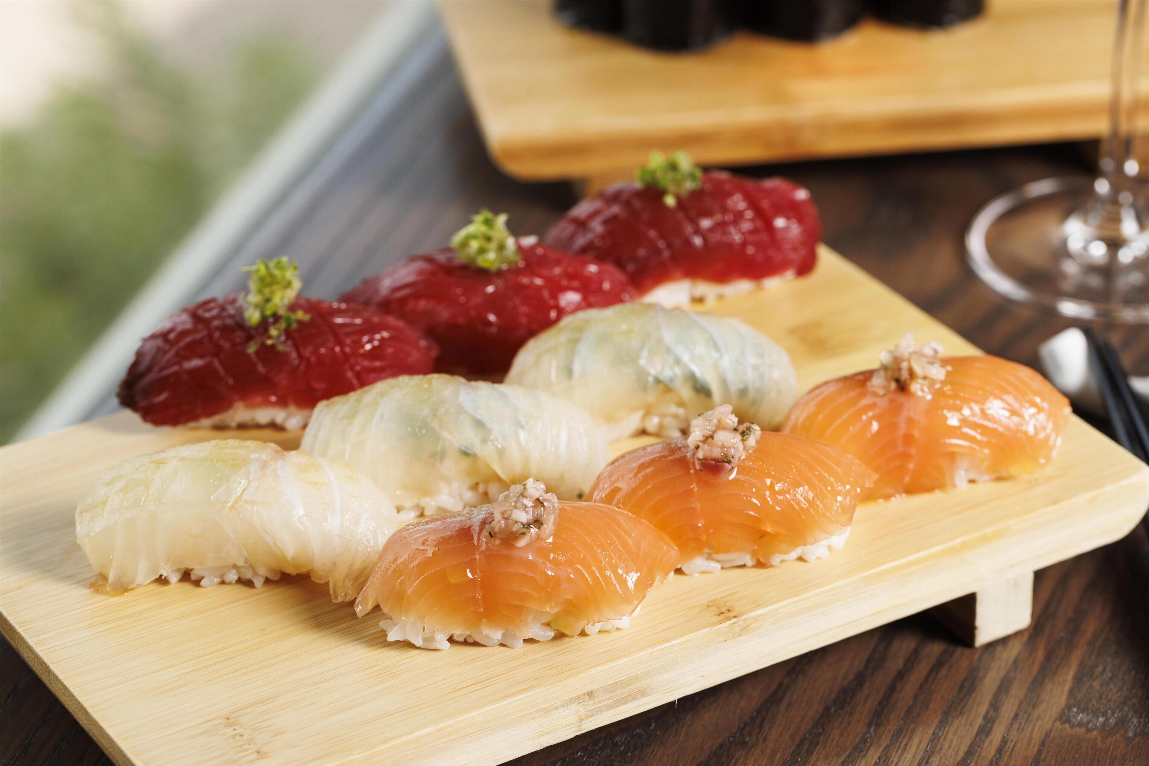 A wooden serving board with various sushi pieces, including salmon and possibly other types of fish, on a wooden table.