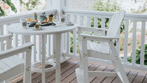 A white wooden porch with a round table and two chairs, a lantern above, and a view of a building in the background. - Grand Hotel (Kennebunk)