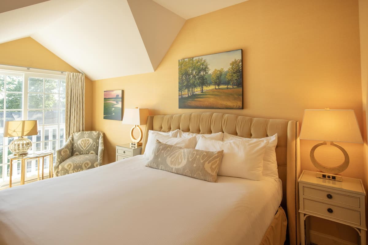 A hotel room with a large bed, two bedside tables, a chair, and a window with curtains.